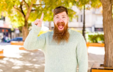 Photo for Red hair bearded man feeling like a happy and excited genius after realizing an idea, cheerfully raising finger, eureka! - Royalty Free Image
