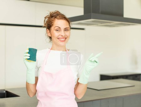 Photo for Young pretty woman smiling cheerfully, feeling happy and pointing to the side. housekeeper concept - Royalty Free Image