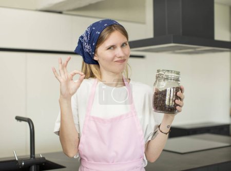 Téléchargez les photos : Jeune jolie femme se sentant heureuse, montrant son approbation avec un geste correct. chef maison avec grains de café - en image libre de droit