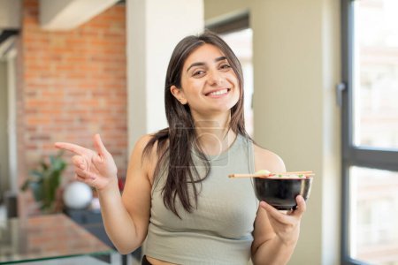 Photo for Young woman smiling cheerfully, feeling happy and pointing to the side. ramen bowl - Royalty Free Image