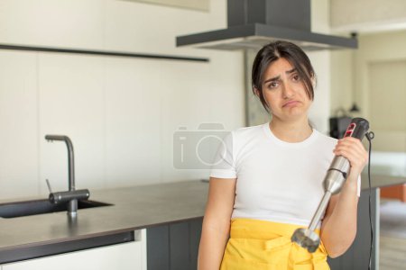 Photo for Young woman feeling sad and whiney with an unhappy look and crying. chef with hand blender - Royalty Free Image