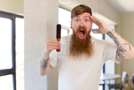 Téléchargez les photos : Homme aux cheveux roux regardant heureux, étonné et surpris avec un peigne à cheveux - en image libre de droit