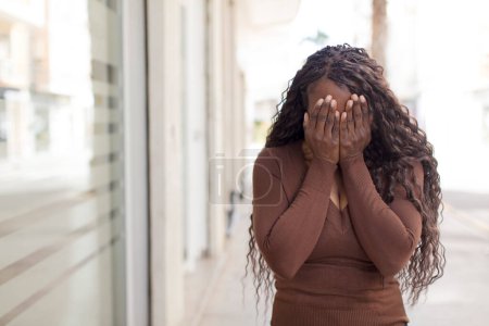Téléchargez les photos : Afro jolie femme noire se sentant triste, frustré, nerveux et déprimé, couvrant le visage avec les deux mains, pleurant - en image libre de droit