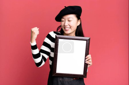 Photo for Young adult pretty asian woman with a beret and an empty picture frame - Royalty Free Image