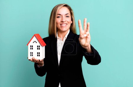 Foto de Bonita mujer rubia sonriendo y buscando amigable, mostrando el número tres. concepto de bienes raíces - Imagen libre de derechos