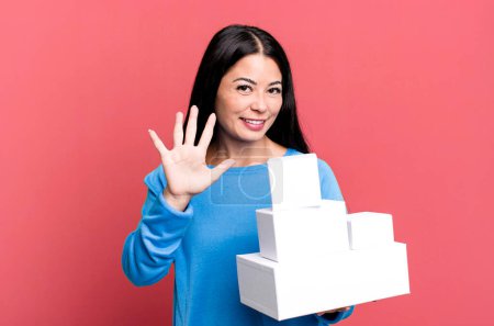 Photo for Hispanic pretty woman smiling and looking friendly, showing number five. with white boxes packagings - Royalty Free Image