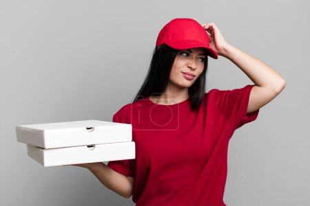 Foto de Mujer bonita hispana sintiéndose desconcertada y confundida, rascándose la cabeza. entrega concepto de pizza - Imagen libre de derechos