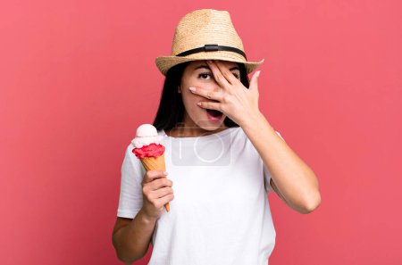 Foto de Mujer bonita hispana mirando sorprendida, asustada o aterrorizada, cubriendo la cara con la mano. helados y concepto de verano - Imagen libre de derechos