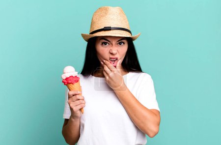 Photo for Hispanic pretty woman with mouth and eyes wide open and hand on chin. ice cream and summer concept - Royalty Free Image