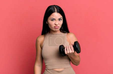 Photo for Hispanic pretty woman feeling puzzled and confused. fitness concept and dumbbell - Royalty Free Image
