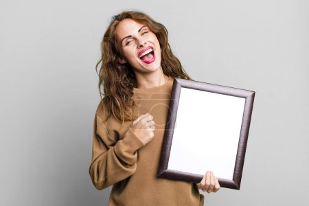 Photo for Hispanic pretty woman feeling happy and facing a challenge or celebrating with an empty blank frame - Royalty Free Image
