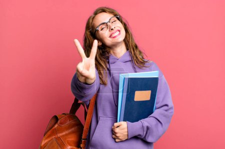 Photo for Hispanic pretty woman smiling and looking happy, gesturing victory or peace. university student concept - Royalty Free Image