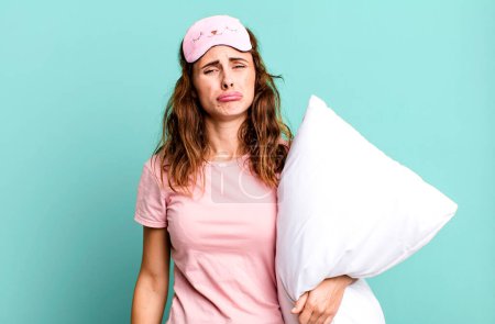 Photo for Hispanic pretty woman feeling sad and whiney with an unhappy look and crying wearing pajamas and a pillow - Royalty Free Image