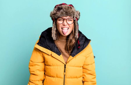 Foto de Mujer bonita hispana sintiéndose disgustada e irritada y la lengua fuera usando anorak. concepto frío e invierno - Imagen libre de derechos