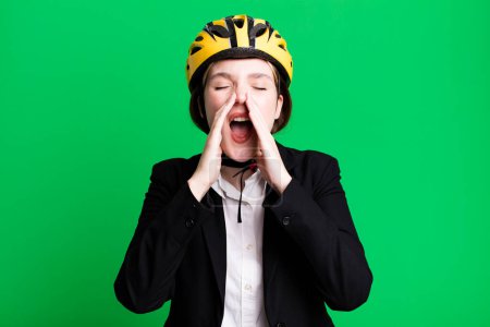 Photo for Young pretty woman feeling happy,giving a big shout out with hands next to mouth. bike and businesswoman concept - Royalty Free Image