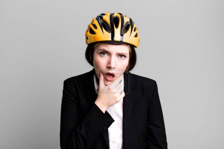 Photo for Young pretty woman with mouth and eyes wide open and hand on chin. bike and businesswoman concept - Royalty Free Image