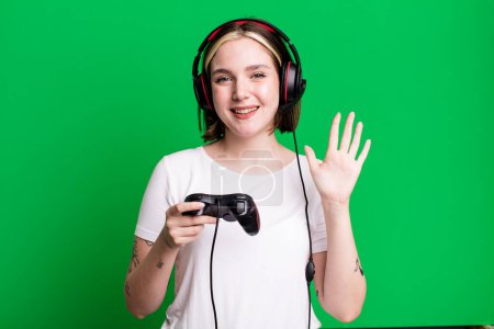 Photo for Young pretty woman smiling happily, waving hand, welcoming and greeting you. gamer concept - Royalty Free Image