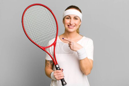 Téléchargez les photos : Jeune jolie femme souriant joyeusement, se sentant heureuse et pointant du doigt le côté. concept de tennis - en image libre de droit