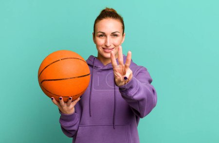 Foto de Joven bonita mujer sonriendo y buscando amigable, mostrando el número tres. concepto de baloncesto - Imagen libre de derechos