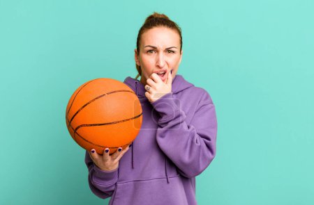 Foto de Joven mujer bonita con la boca y los ojos bien abiertos y la mano en la barbilla. concepto de baloncesto - Imagen libre de derechos