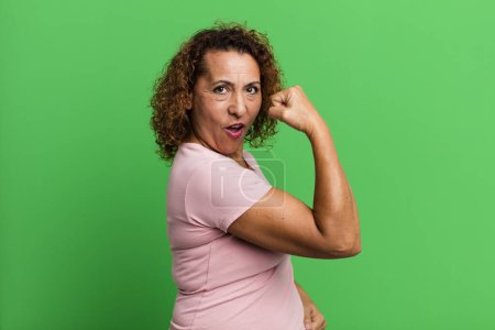 Téléchargez les photos : Femme hispanique d'âge moyen se sentant heureuse, satisfaite et puissante, flexion ajustement et biceps musculaires, regardant fort après la salle de gym - en image libre de droit