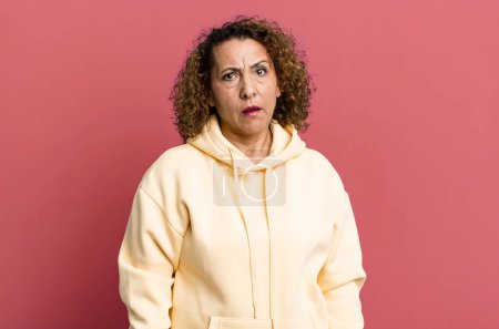 Photo for Middle age hispanic woman feeling puzzled and confused, with a dumb, stunned expression looking at something unexpected - Royalty Free Image