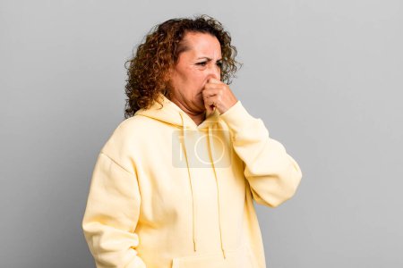 Photo for Middle age hispanic woman feeling disgusted, holding nose to avoid smelling a foul and unpleasant stench - Royalty Free Image