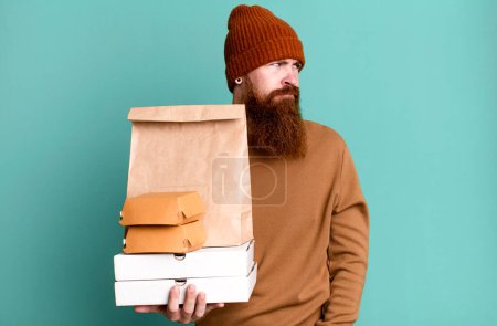 Foto de Joven adulto pelo rojo barbudo hombre fresco con una bolsa de papel con comida para llevar - Imagen libre de derechos