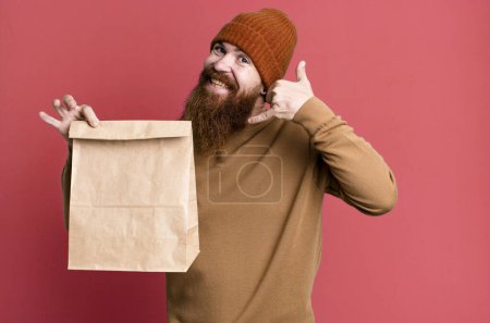 Photo for Young adult red hair bearded cool man with a paper bag with take away food - Royalty Free Image