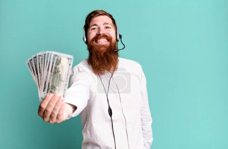 Téléchargez les photos : Jeune adulte cheveux roux barbu cool agent homme avec casque et billets en dollars - en image libre de droit