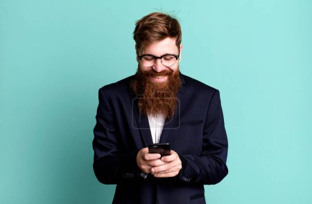 Téléchargez les photos : Jeune adulte cheveux roux barbu cool homme d'affaires en utilisant son smartphone - en image libre de droit