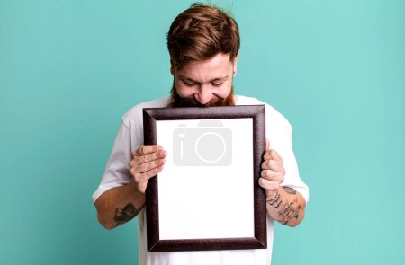 Foto de Joven adulto pelo rojo barbudo fresco hombre sosteniendo un cuadro vacío marco - Imagen libre de derechos