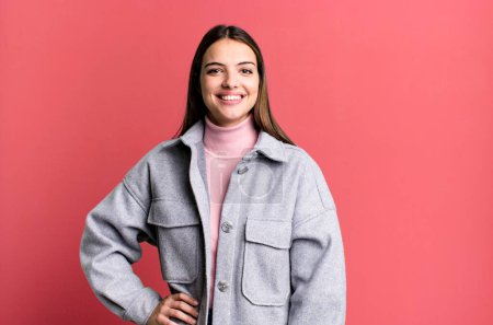 Photo for Pretty young adult woman smiling happily with a hand on hip and confident, positive, proud and friendly attitude - Royalty Free Image