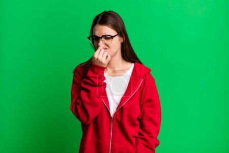 Téléchargez les photos : Jolie jeune femme adulte se sentant dégoûtée, tenant le nez pour éviter de sentir une odeur nauséabonde et désagréable - en image libre de droit