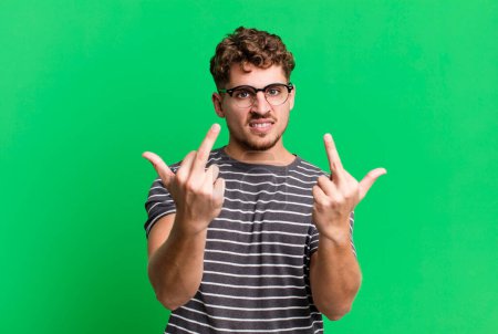 Foto de Young adult caucasian man feeling provocative, aggressive and obscene, flipping the middle finger, with a rebellious attitude - Imagen libre de derechos