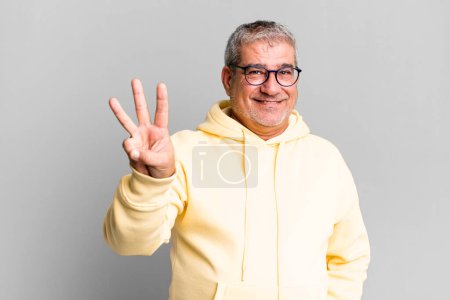 Téléchargez les photos : Homme âgé d'âge moyen souriant et regardant amical, montrant numéro trois ou troisième avec la main vers l'avant, compte à rebours - en image libre de droit