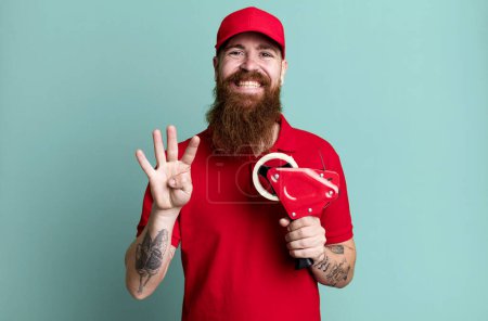 Foto de Barba larga hombre sonriendo y buscando amigable, mostrando el número cuatro. concepto de empaquetador de envío - Imagen libre de derechos