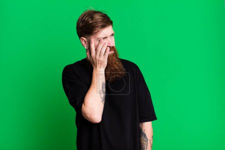 Téléchargez les photos : Barbe longue et cheveux roux homme se sentant ennuyé, frustré et somnolent après une fatigante - en image libre de droit