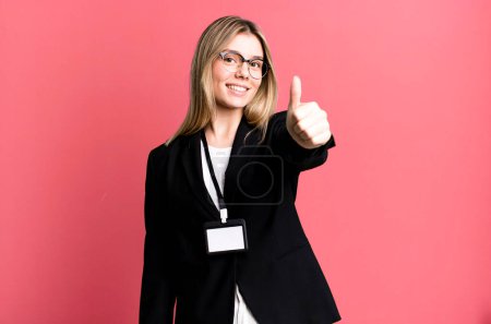 Téléchargez les photos : Jeune jolie femme se sentant fière, souriant positivement avec les pouces levés. carte d'identité concept d'accréditation - en image libre de droit