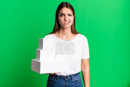 Téléchargez les photos : Jeune jolie femme à l'air perplexe et confus. boîtes blanches vierges - en image libre de droit