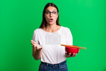 Photo for Young pretty woman amazed, shocked and astonished with an unbelievable surprise. japanese ramen noodles concept - Royalty Free Image
