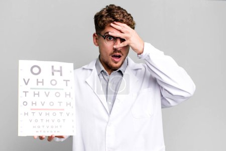 Photo for Young adult caucasian man looking shocked, scared or terrified, covering face with hand. optical vision test concept - Royalty Free Image