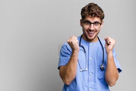 Téléchargez les photos : Jeune homme caucasien adulte se sentant choqué, riant et célébrant le succès. concept d'infirmière - en image libre de droit
