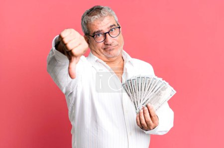 Photo for Middle age senior man feeling cross,showing thumbs down. dollar banknotes concept - Royalty Free Image