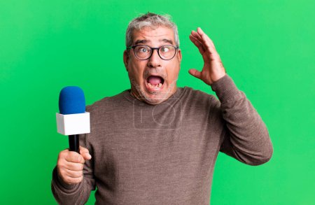 Foto de Hombre mayor de mediana edad gritando con las manos en alto. periodista o presentador de televisión con un micro - Imagen libre de derechos