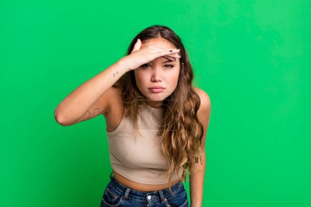 Photo for Young pretty woman looking bewildered and astonished, with hand over forehead looking far away, watching or searching - Royalty Free Image