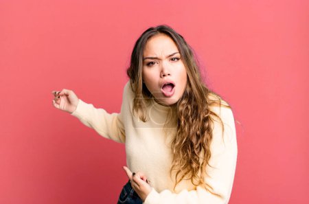 Photo for Young pretty woman feeling shocked and surprised, pointing to copy space on the side with amazed, open-mouthed look - Royalty Free Image