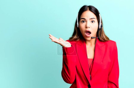 Photo for Hispanic pretty woman looking surprised and shocked, with jaw dropped holding an object. telemarketing concept - Royalty Free Image