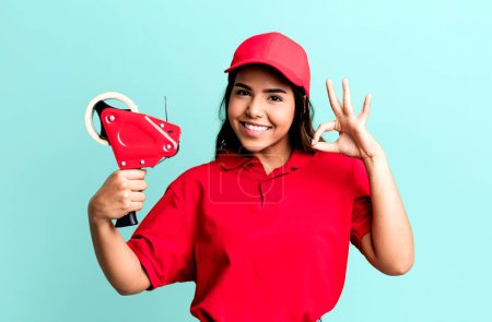 Photo for Hispanic pretty woman feeling happy, showing approval with okay gesture. packer and delivery employee - Royalty Free Image