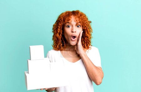 Photo for Red hair pretty woman feeling shocked and scared. blank packages boxes concept - Royalty Free Image